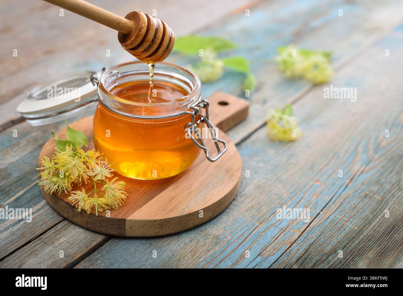 Miele di tiglio in vaso di vetro con dipper di miele di legno e fiori di tiglio su fondo di legno Foto Stock
