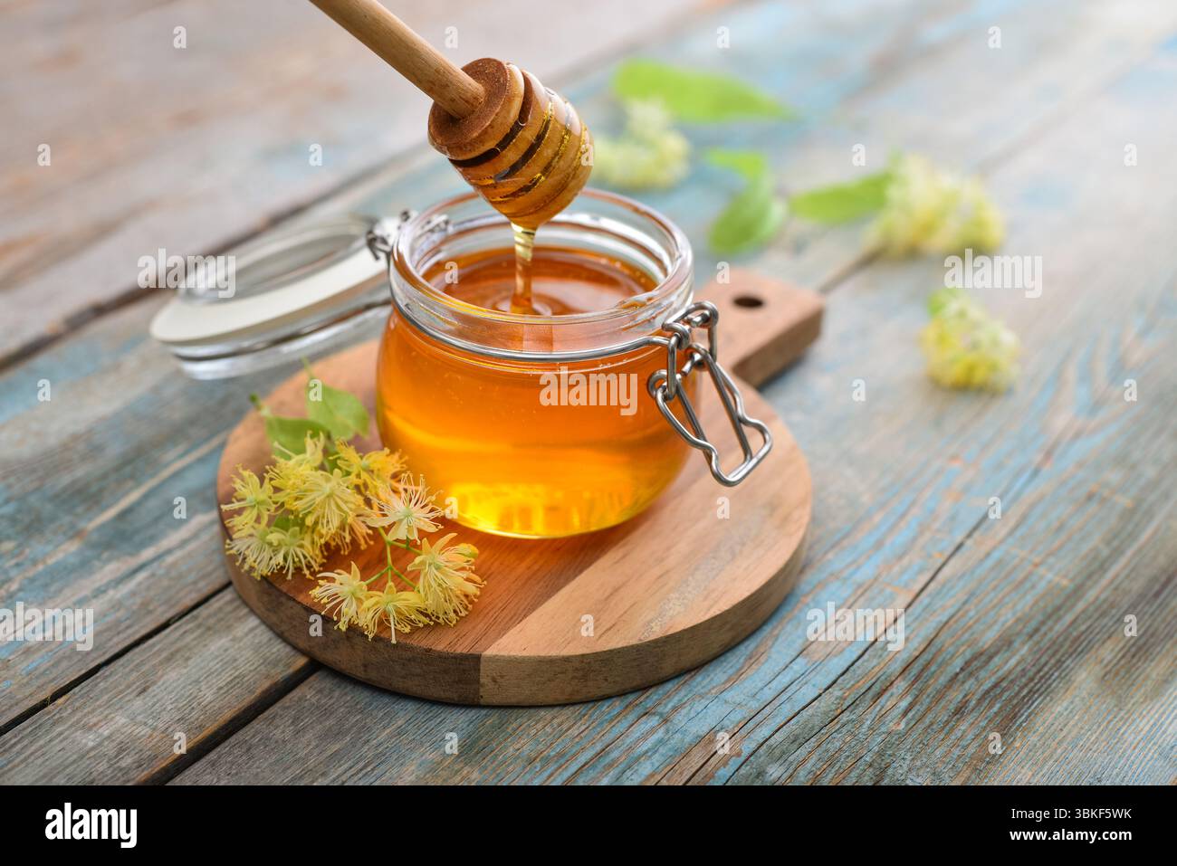 Miele di tiglio in vaso di vetro con dipper di miele di legno e fiori di tiglio su fondo di legno Foto Stock