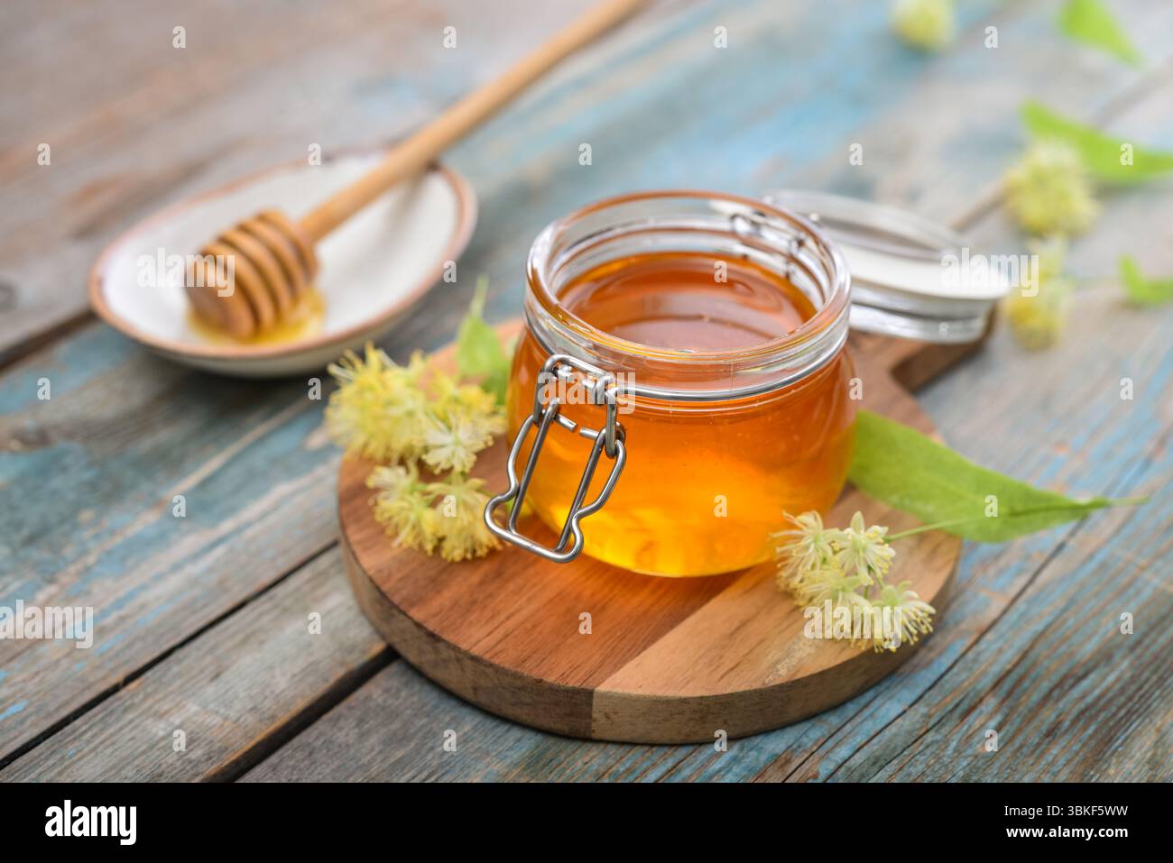 Miele di tiglio in vaso di vetro con dipper di miele di legno e fiori di tiglio su fondo di legno Foto Stock