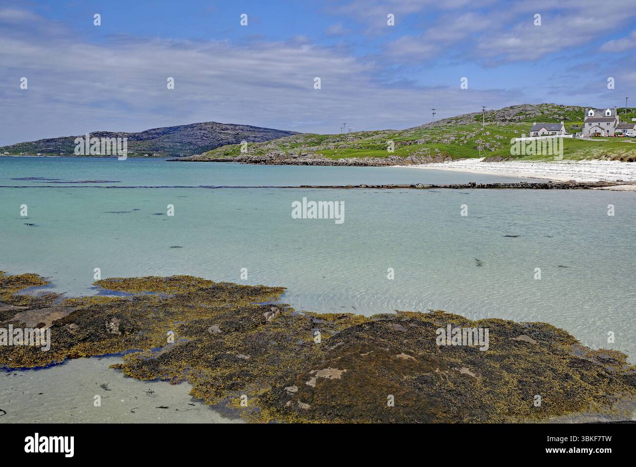 Acque cristalline e una spiaggia tranquilla con colline e case sullo sfondo sotto un cielo parzialmente nuvoloso, Eriksay, Ebridi, Scozia, Regno Unito, Europa Foto Stock