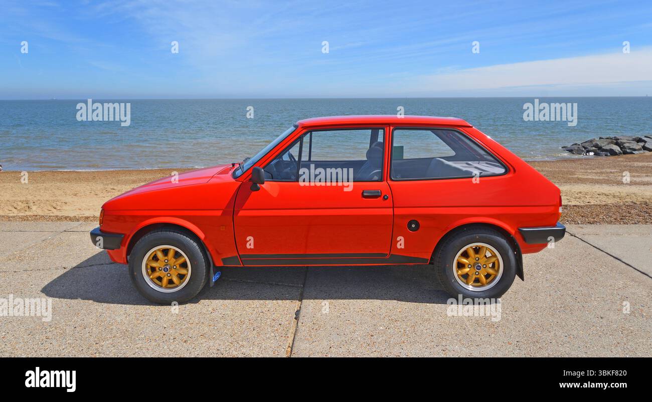 Classica Red Ford Fiesta parcheggiata sulla spiaggia lungomare e sul mare sullo sfondo. Foto Stock