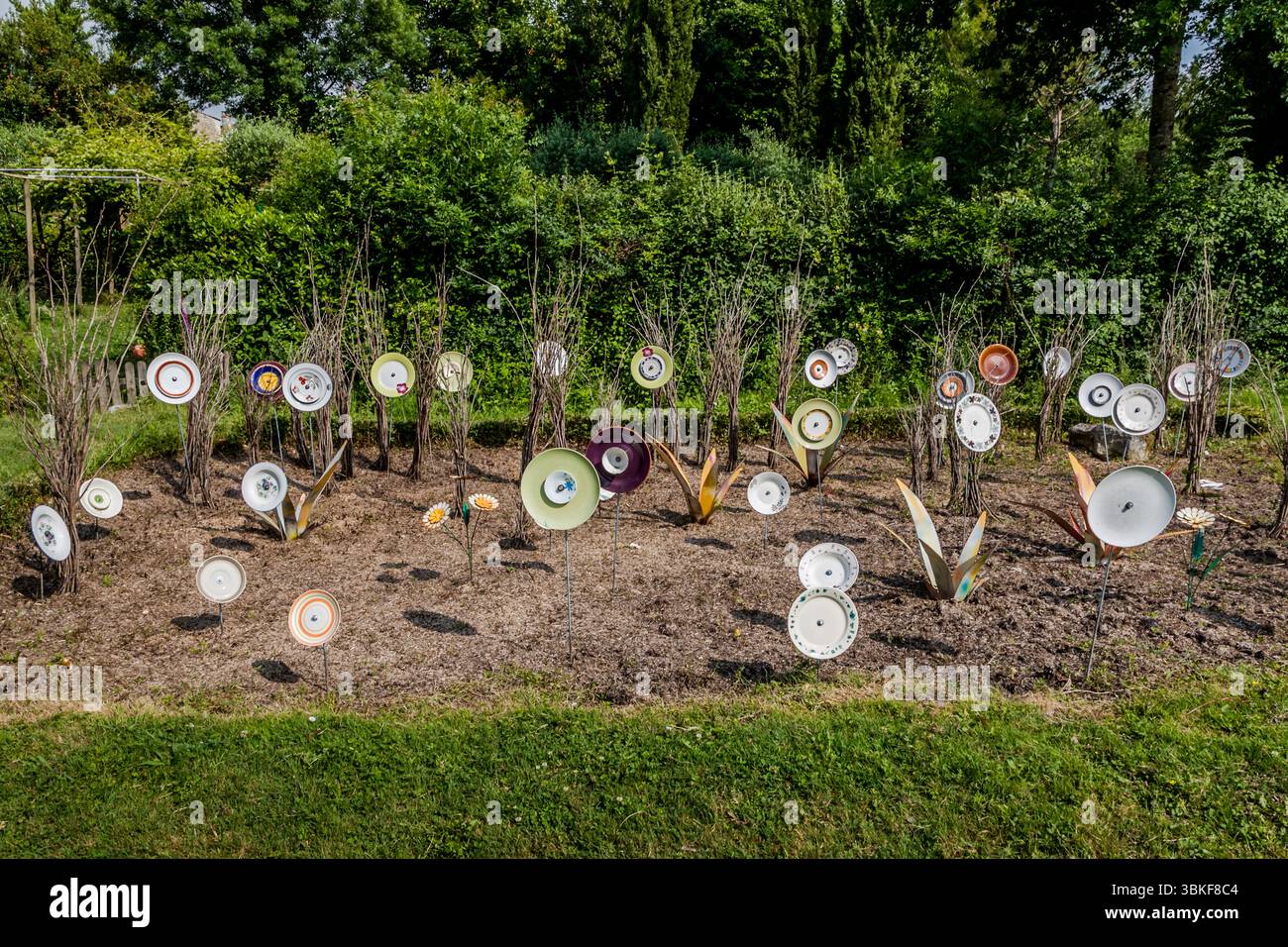 Piatti su pali in un giardino frontale in Francia, Nouvelle-Aquitaine. Il motivo si inserisce nel proverbio tedesco "Über den Tellerrand schauen" (guarda oltre il bordo del piatto), che si riferisce a un atteggiamento aperto e curioso in cui si è disposti a trascendere i propri confini e ad imparare cose nuove. La frase è spesso usata in connessione con il cosmopolitismo, un cambiamento di prospettiva o innovazione. Pensare fuori dagli schemi. L'installazione decorativa del giardino comprende vari pezzi di stoviglie attaccati ai bastoncini e collocati in un letto di fiori per creare una scena giocosa e artistica. L'installazione è Foto Stock