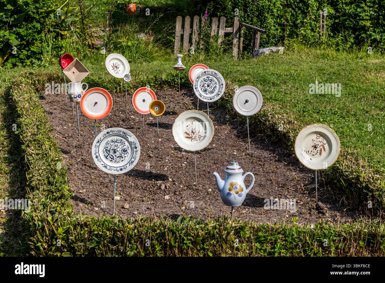 Piatti su pali in un giardino frontale in Francia, Nouvelle-Aquitaine. Il motivo si inserisce nel proverbio tedesco "Über den Tellerrand schauen" (guarda oltre il bordo del piatto), che si riferisce a un atteggiamento aperto e curioso in cui si è disposti a trascendere i propri confini e ad imparare cose nuove. La frase è spesso usata in connessione con il cosmopolitismo, un cambiamento di prospettiva o innovazione. Pensare fuori dagli schemi. L'installazione decorativa del giardino comprende vari pezzi di stoviglie attaccati ai bastoncini e collocati in un letto di fiori per creare una scena giocosa e artistica. L'installazione è Foto Stock