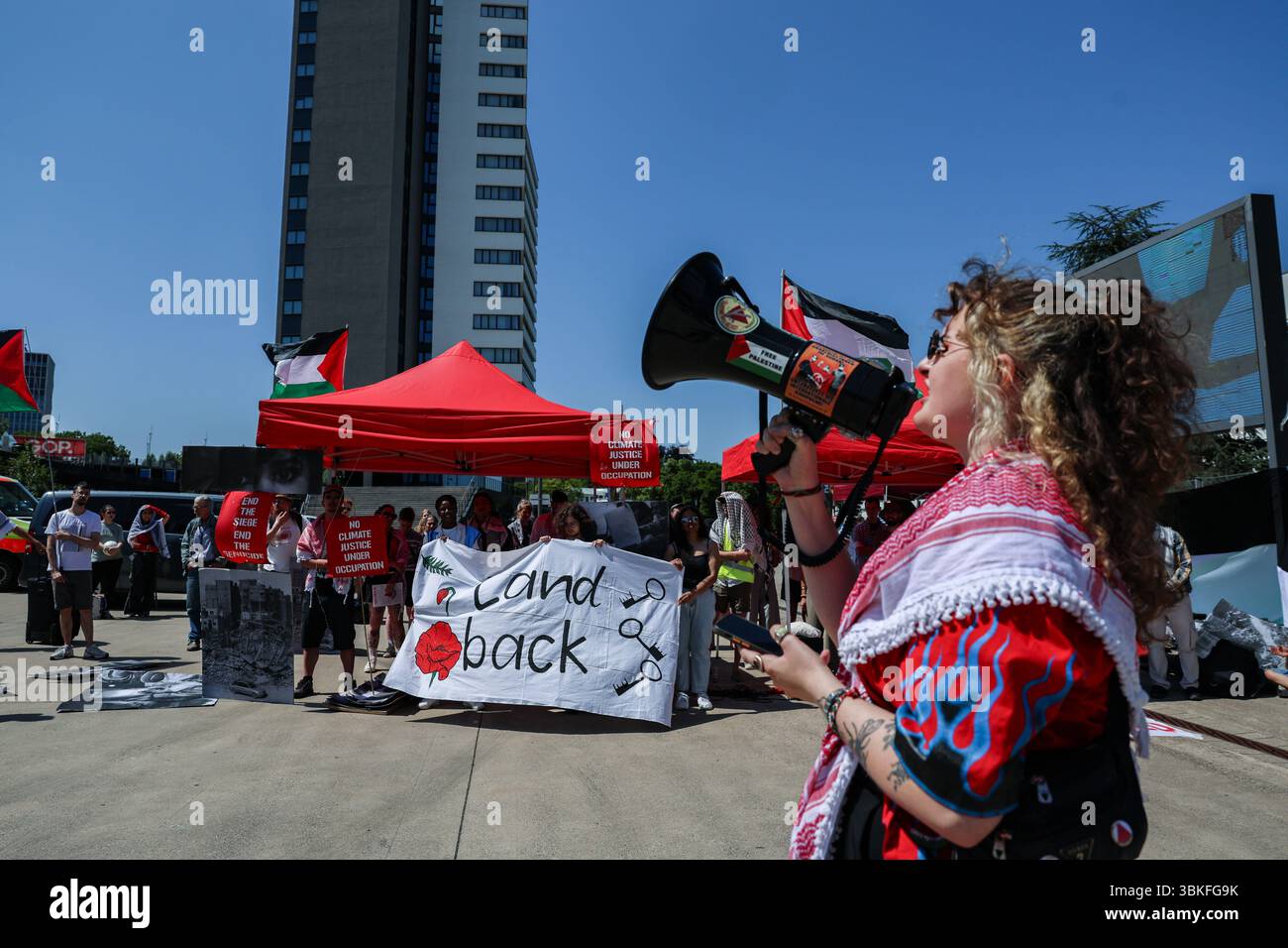 Bonn, Germania, Germania. 19 giugno 2025. Un manifestante si rivolge a una folla di corno al di fuori del World Conference Center di Bonn durante i colloqui sul clima SB62, amplificando gli appelli alla sovranità indigena e alla solidarietà palestinese. La bandiera "Land Back” e le bandiere alzate evidenziano l'intersezione tra giustizia climatica, decolonizzazione e diritti umani al centro della protesta. (Credit Image: © Bianca Otero/ZUMA Press Wire) SOLO PER USO EDITORIALE! Non per USO commerciale! Foto Stock