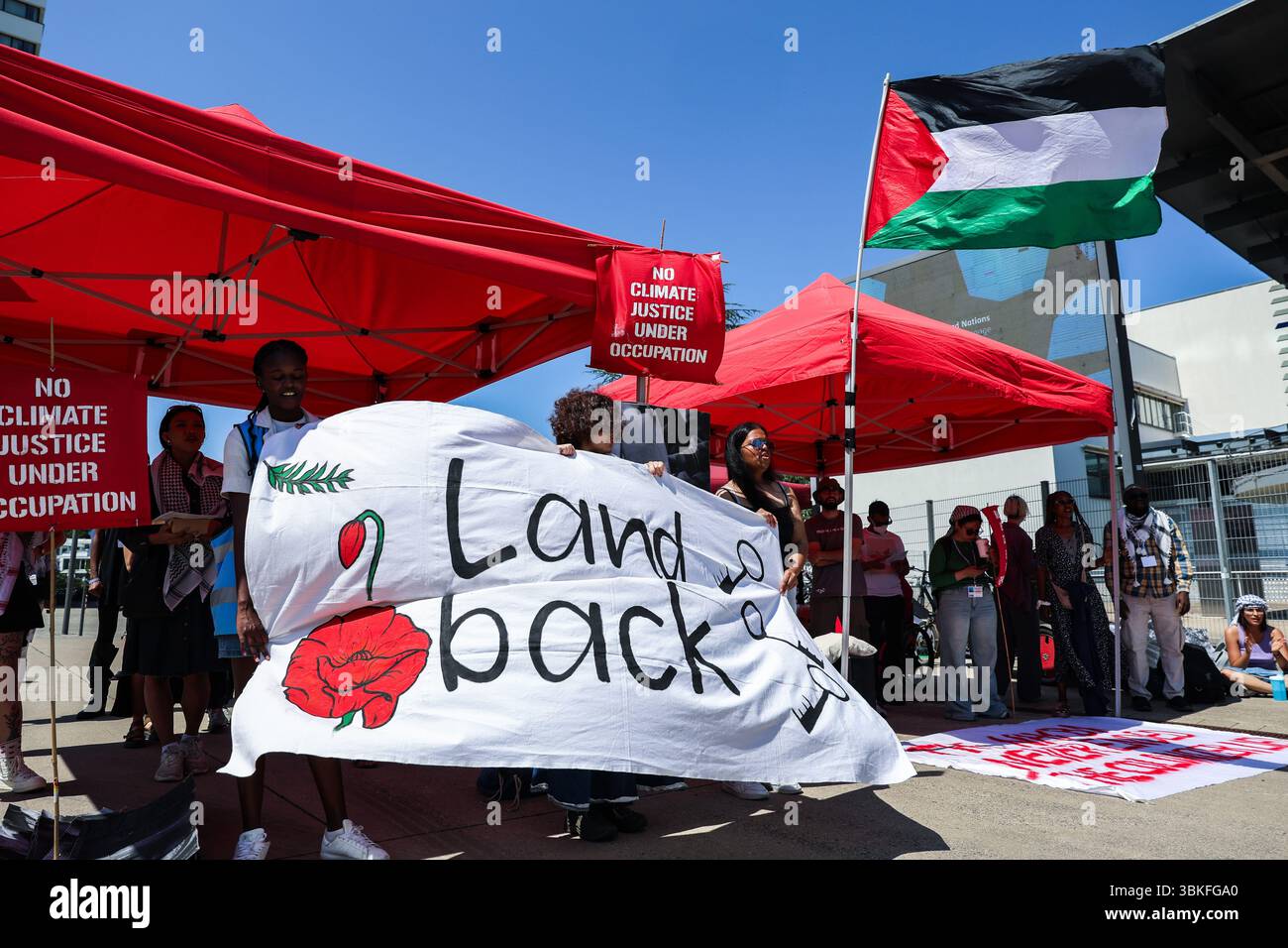 Bonn, Germania, Germania. 19 giugno 2025. Protesta morbida al di fuori del World Conference Center di Bonn durante i colloqui sul clima SB62, amplificando le richieste di sovranità indigena e solidarietà palestinese. Il banner "Land Back”, i manifesti di "No Climate Justice under Occupationmand Raised Flags”, evidenziano l'intersezione tra giustizia climatica, decolonizzazione e diritti umani al centro della protesta. (Credit Image: © Bianca Otero/ZUMA Press Wire) SOLO PER USO EDITORIALE! Non per USO commerciale! Foto Stock