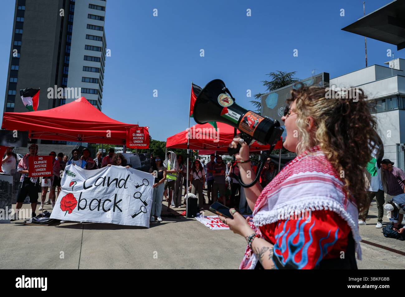 Bonn, Germania, Germania. 19 giugno 2025. Un manifestante si rivolge a una folla di corno al di fuori del World Conference Center di Bonn durante i colloqui sul clima SB62, amplificando gli appelli alla sovranità indigena e alla solidarietà palestinese. La bandiera "Land Back” e le bandiere alzate evidenziano l'intersezione tra giustizia climatica, decolonizzazione e diritti umani al centro della protesta. (Credit Image: © Bianca Otero/ZUMA Press Wire) SOLO PER USO EDITORIALE! Non per USO commerciale! Foto Stock