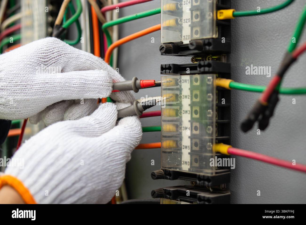 Un ingegnere dell'alimentazione sta lavorando alla sottostazione, collegando accuratamente i fili con precisione. il collaboratore indossa guanti protettivi per garantire la sicurezza durante la mano Foto Stock