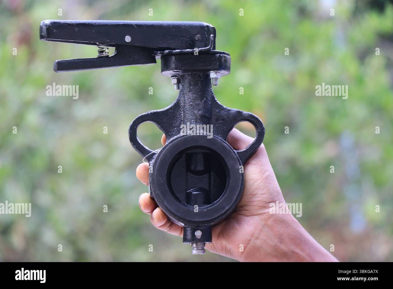 Valvola a farfalla in metallo fuso utilizzato per controllare il flusso di fluidi tenuti in mano su sfondo naturale Foto Stock