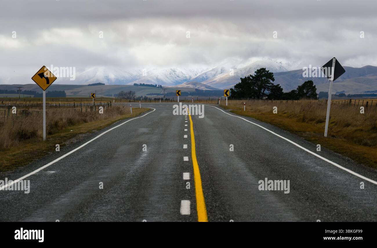 Segui le indicazioni per Winding Road. Montagne innevate in lontananza. Centro di Otago. Isola del Sud. Nuova Zelanda. Foto Stock