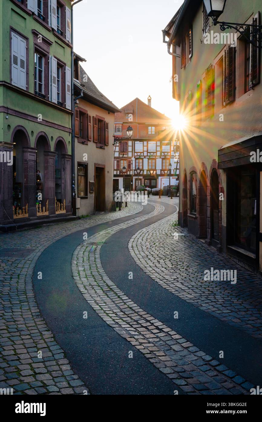 Il sole tramonta splende tra case a graticcio attraverso un vicolo tortuoso nel centro storico di Ribeauvillé, in Alsazia Foto Stock