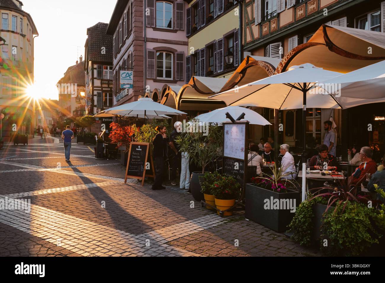 Ribeauvillé, Alsazia, Francia: Ospiti sulla terrazza della Brasserie la Post nel vicolo medievale con case a graticcio retroilluminate dal tramonto Foto Stock