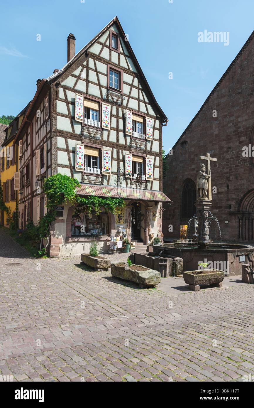 Colorata casa a graticcio, la Fontana di Costantino e la Chiesa di Santa Croce in piazza Jean Ittel nella città vecchia di Kaysersberg, Alsazia, Francia Foto Stock