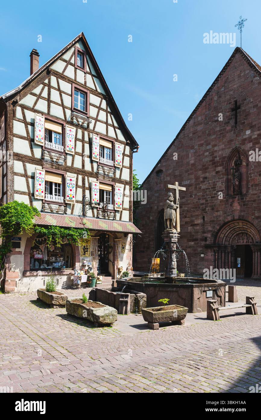 Colorata casa a graticcio, la Fontana di Costantino e la Chiesa di Santa Croce in piazza Jean Ittel nella città vecchia di Kaysersberg, Alsazia, Francia Foto Stock