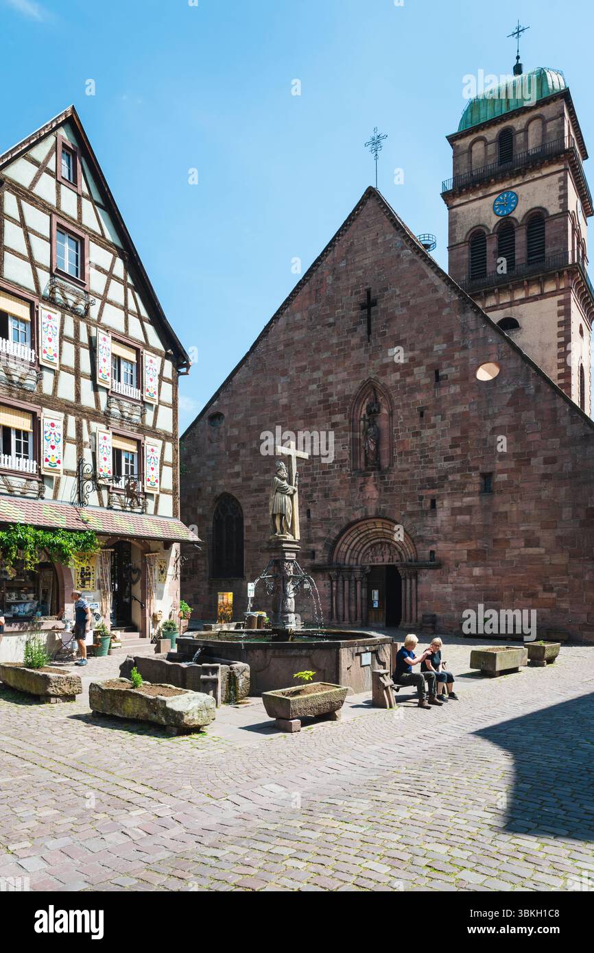 Colorata casa a graticcio, la Fontana di Costantino e la Chiesa di Santa Croce in piazza Jean Ittel nella città vecchia di Kaysersberg, Alsazia, Francia Foto Stock