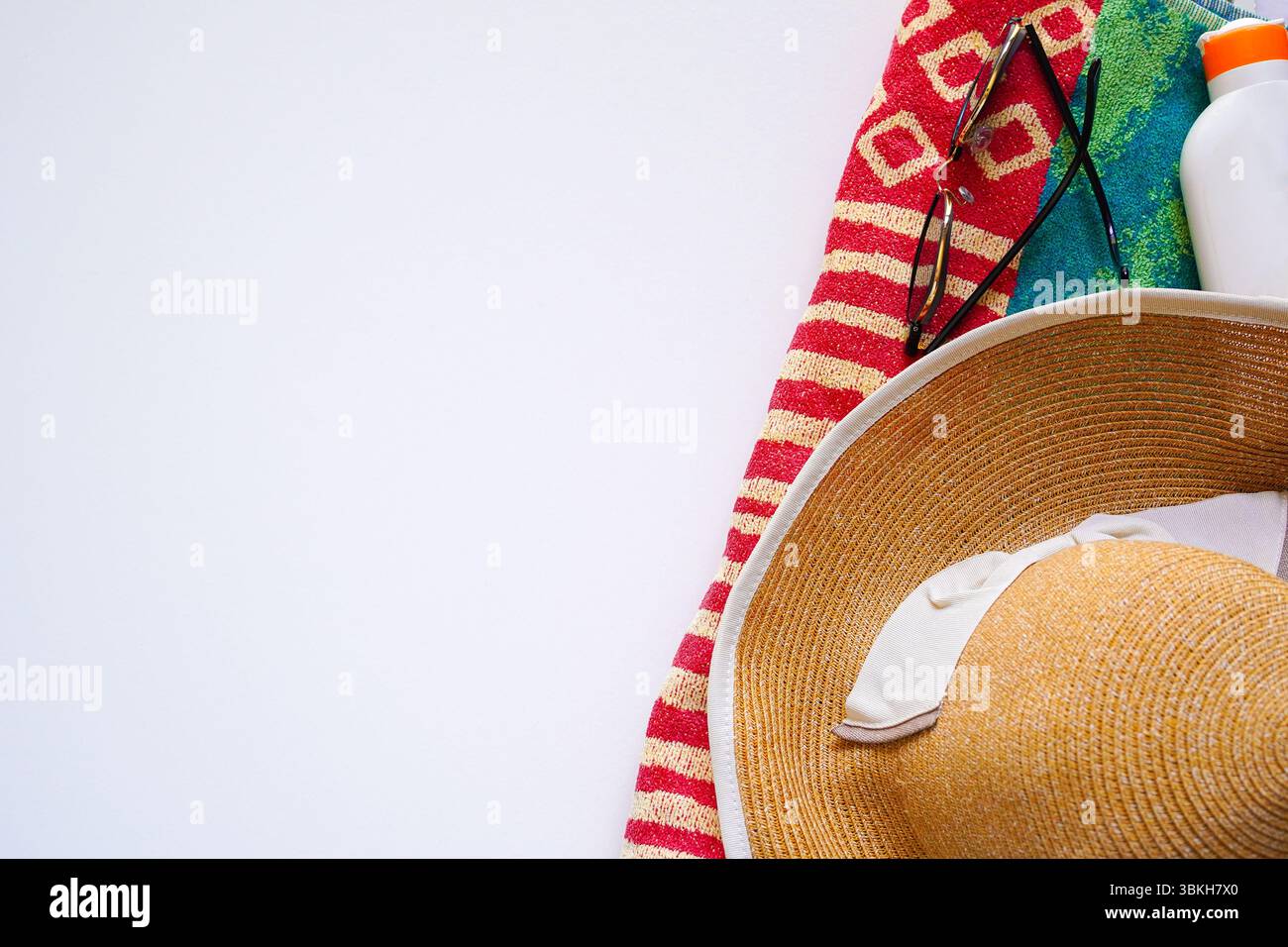 Cappello di paglia e occhiali da sole su sfondo bianco con telo da bagno e crema solare, vacanze estive, foto di nuoto Foto Stock