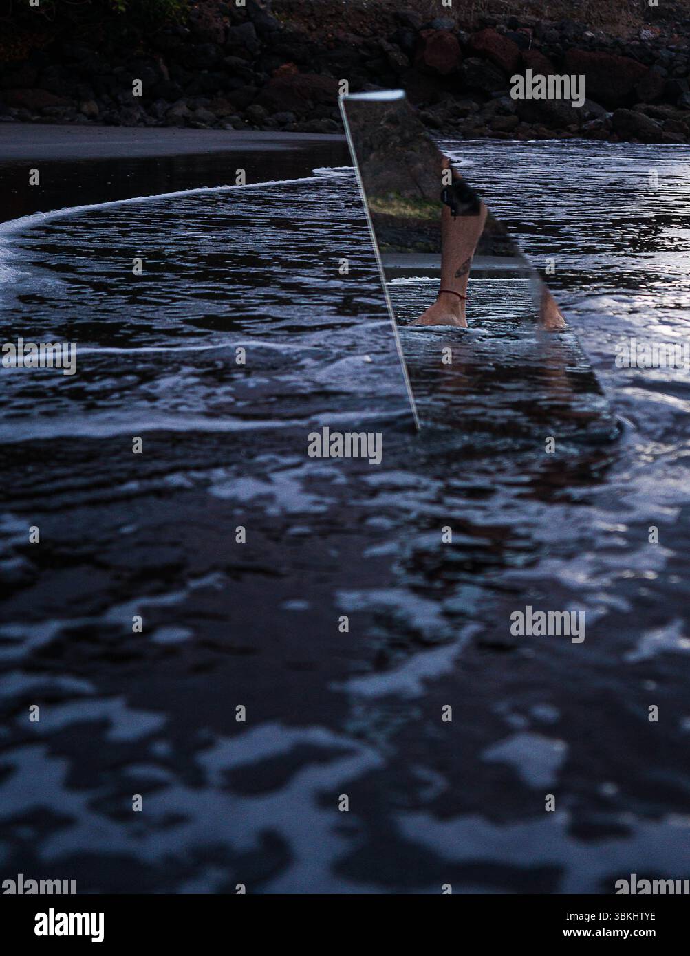 Una persona è in piedi in acqua con un oggetto triangolare, possibilmente una tavola da surf o un'opera d'arte. La scena è misteriosa e intrigante. Foto Stock