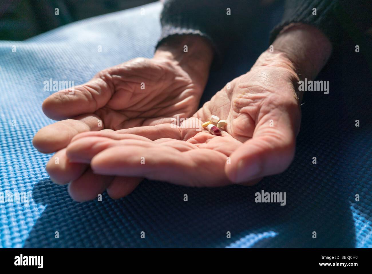 Mani senior con varie pillole appoggiate su un tappetino blu, illuminato dalla calda luce naturale del sole Foto Stock
