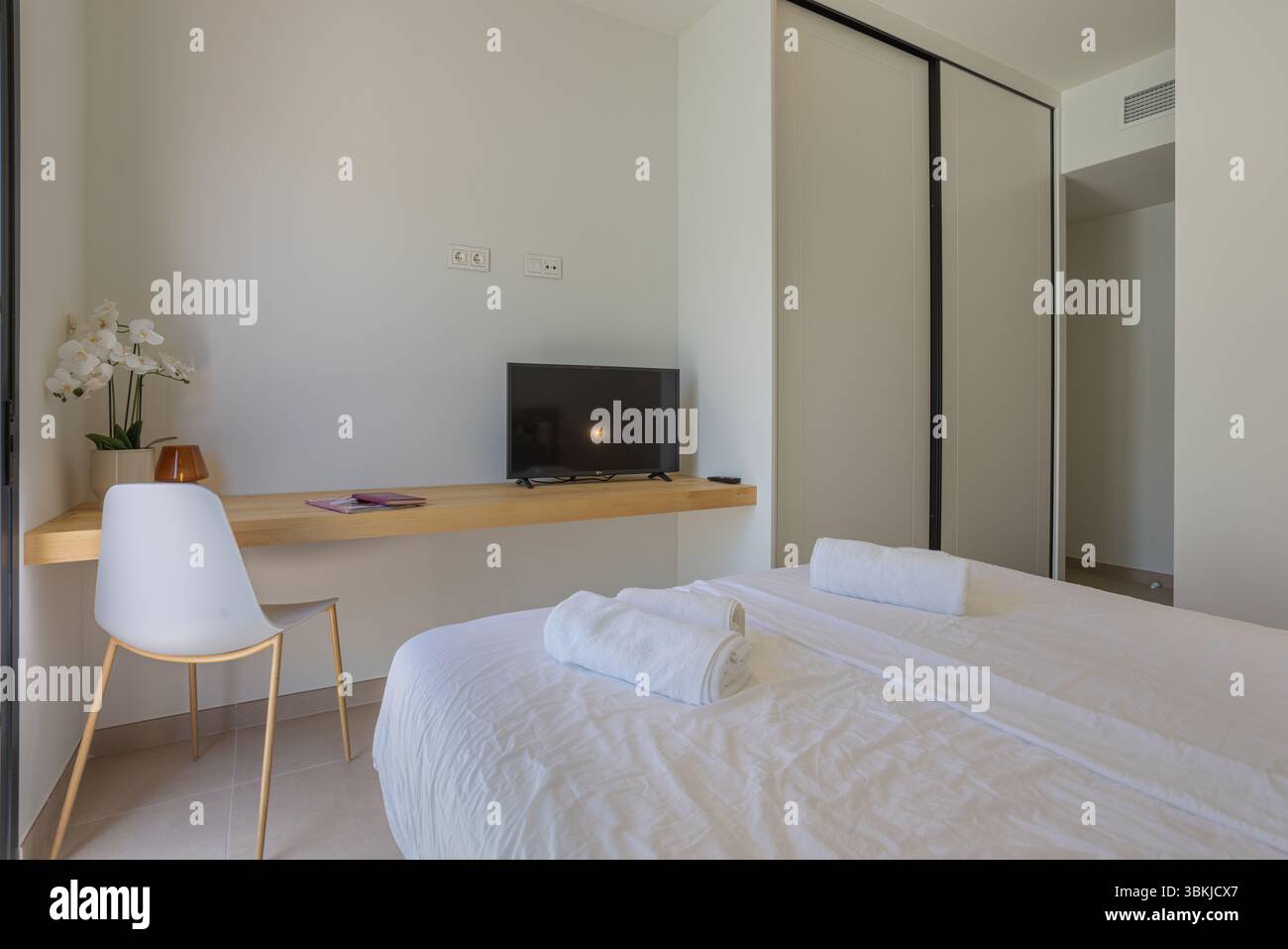 Camera da letto semplice e pulita con lenzuola bianche, TV a schermo piatto e armadio scorrevole. Foto Stock
