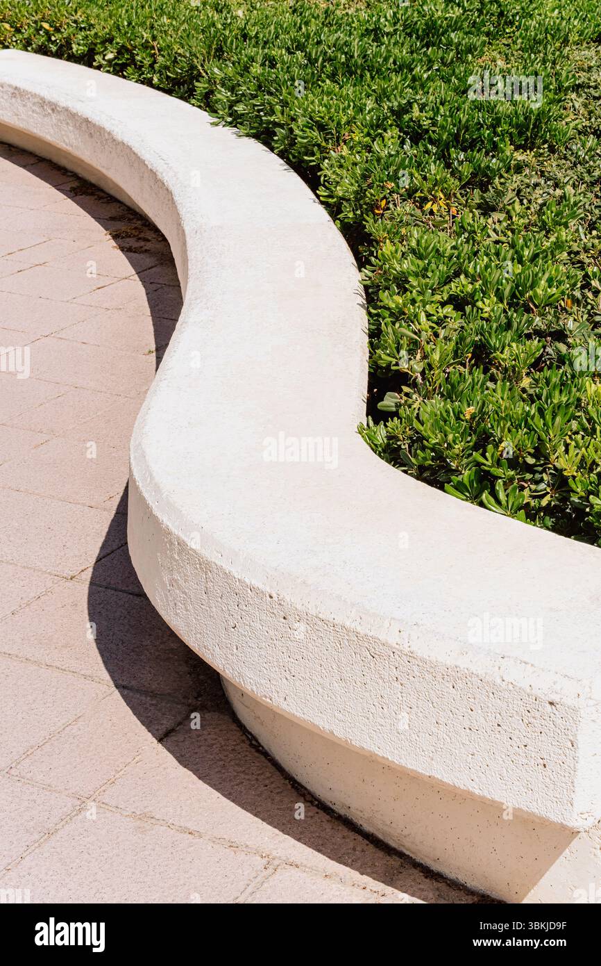 Panca in cemento curvo minimalista nel parco, verde all'interno, architettura paesaggistica e design urbano degli spazi pubblici Foto Stock