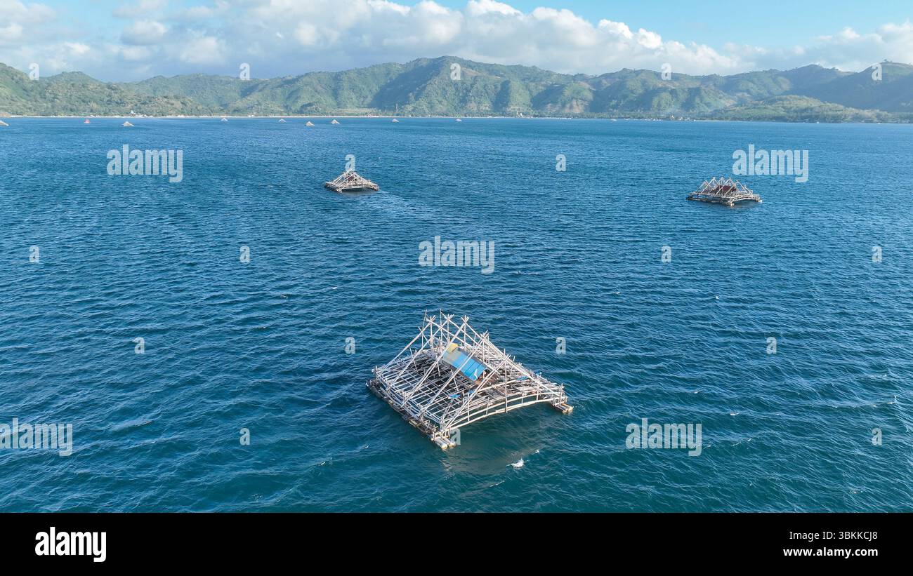 Le piattaforme di pesca di bambù punteggiano il mare blu profondo vicino a Lombok. L'immagine mette in evidenza le forme geometriche e il paesaggio montuoso delle isole. Foto Stock