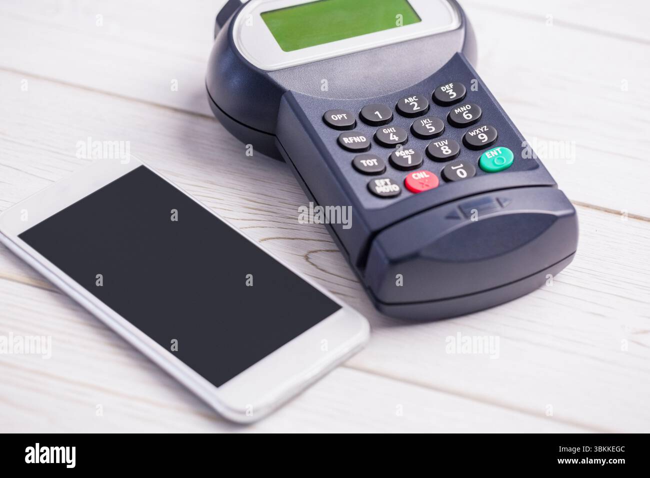 Il terminale POS con tastiera e display è posizionato accanto allo smartphone su un piano portapaziente in legno, dal design piatto Foto Stock