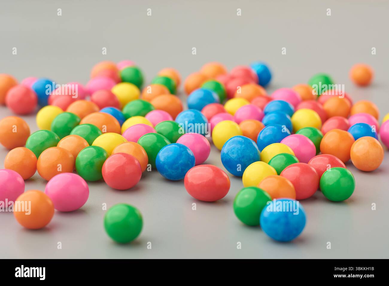 latte sparsi, vivace e colorato, caramelle o ciottoli ricoperti di dolci su sfondo grigio, primo piano di snack dolciumi con messa a fuoco morbida e spazio di copia Foto Stock
