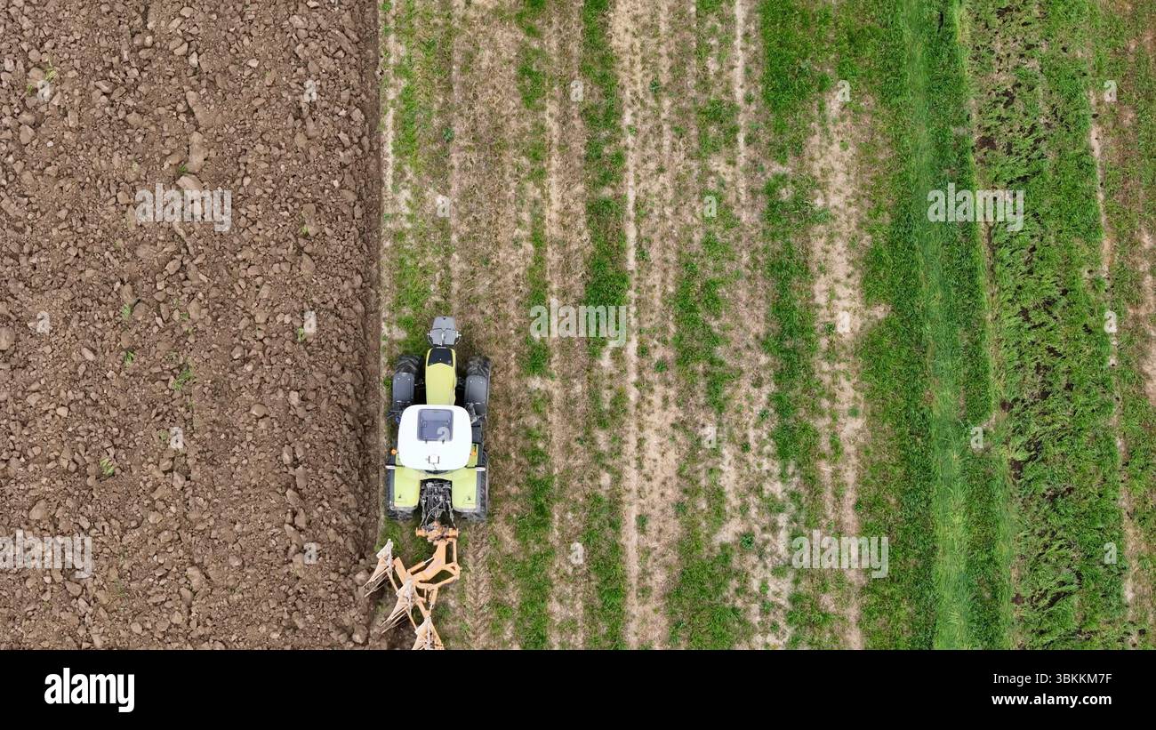 Paesaggio agricolo caratterizzato da un trattore che coltiva un campo di terreno e da colture verdi vibranti che creano un ricco arazzo di texture e motivi Foto Stock
