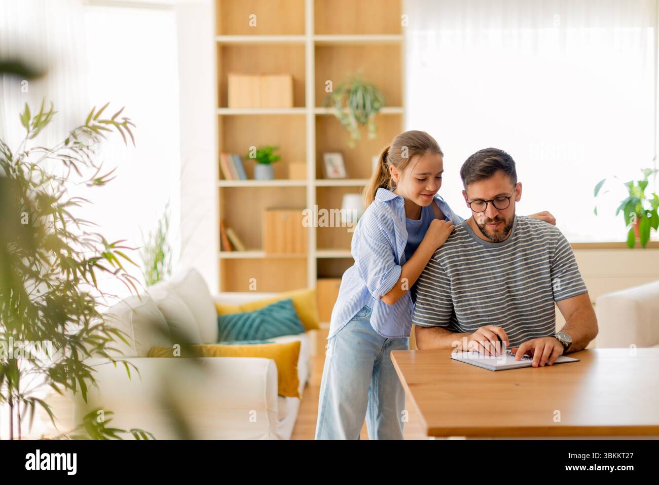 Un padre ama trascorrere un po' di tempo con sua figlia mentre si dedicano alle attività di scrittura in un soggiorno splendidamente progettato con luce naturale. Foto Stock