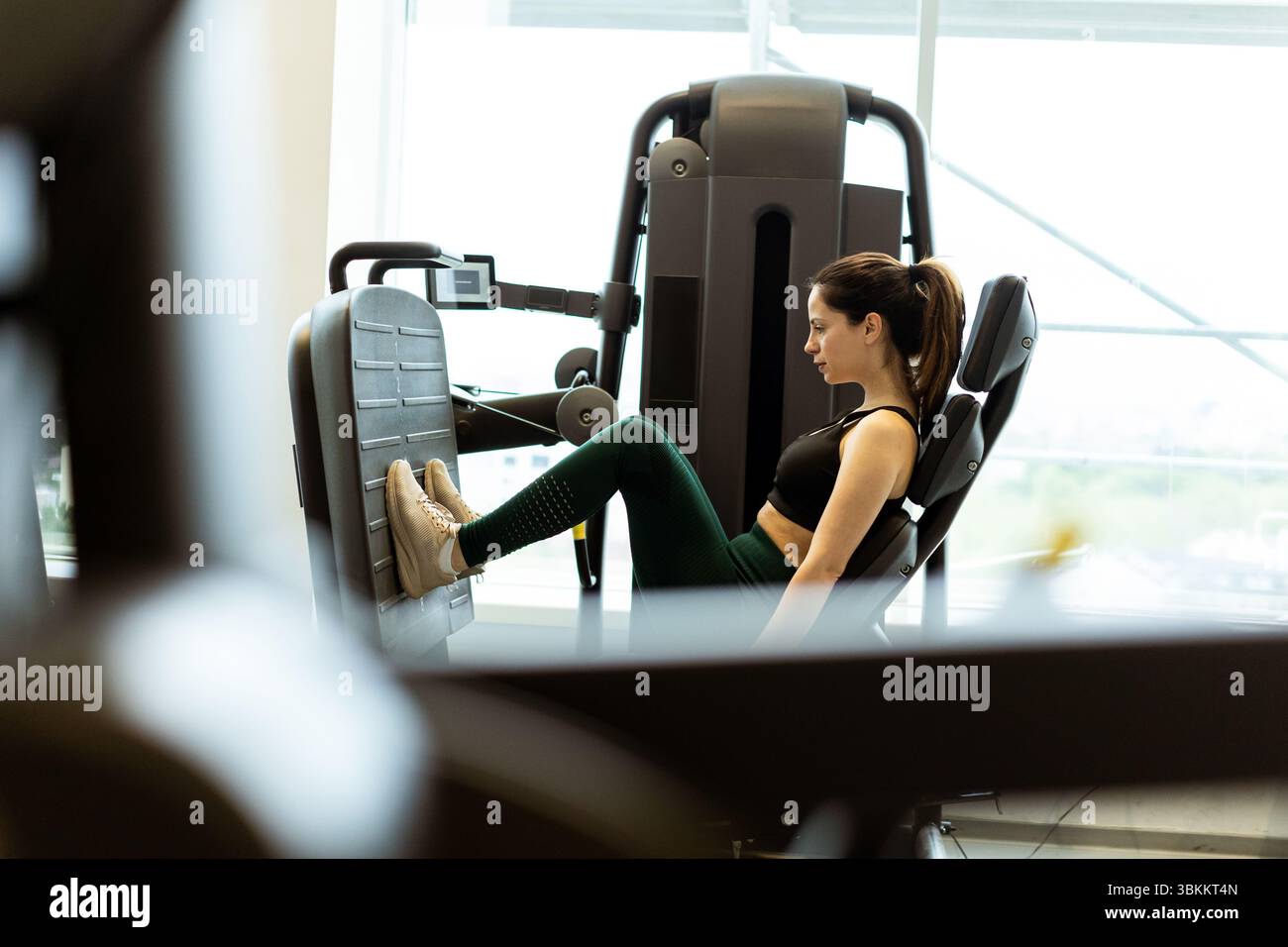 Una donna concentrata si impegna in un esercizio di pressione sulle gambe, amplificando la sua routine di allenamento della forza in un luminoso centro fitness. Foto Stock Una donna concentrata si impegna in un esercizio di pressione sulle gambe, amplificando la sua routine di allenamento della forza in un luminoso centro fitness. Foto Stock