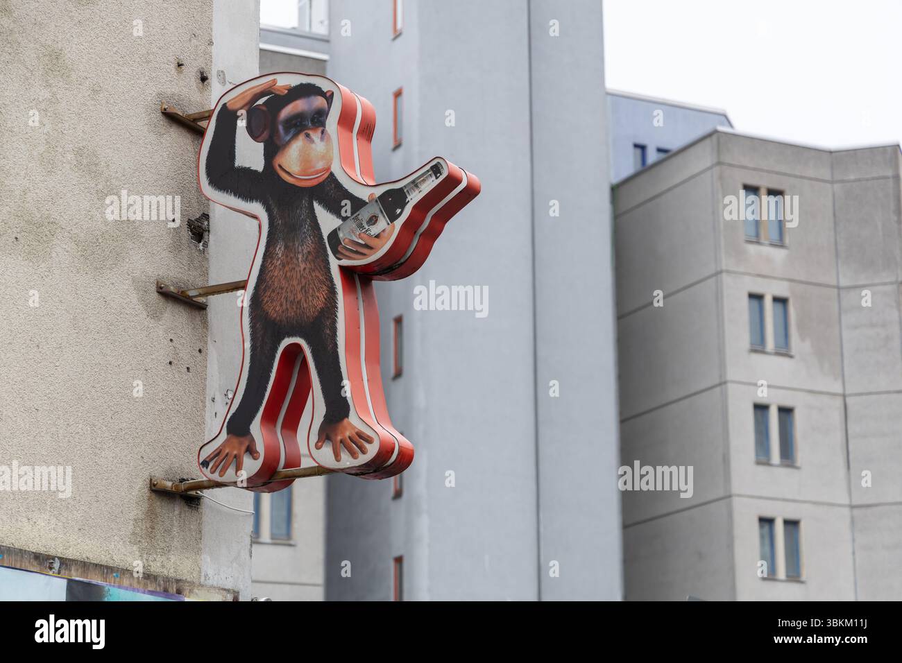 Simpatico segno di uno scimpanzé cartoni animati che tiene in mano una bottiglia di birra, montato su un muro urbano ruvido. Decorazioni da strada divertenti e bizzarre con un'atmosfera vintage. Foto Stock
