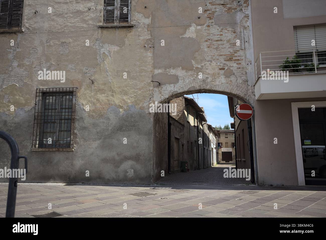 Vicolo all'ombra con un negozio abbandonato alla fine visto da un arco all'inizio della strada in una giornata di sole in una città italiana Foto Stock