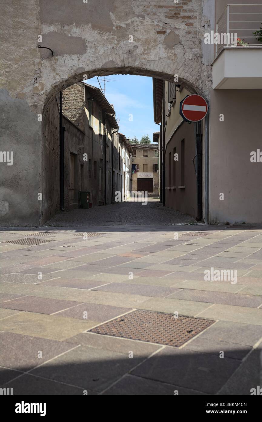 Vicolo all'ombra con un negozio abbandonato alla fine visto da un arco all'inizio della strada in una giornata di sole in una città italiana Foto Stock