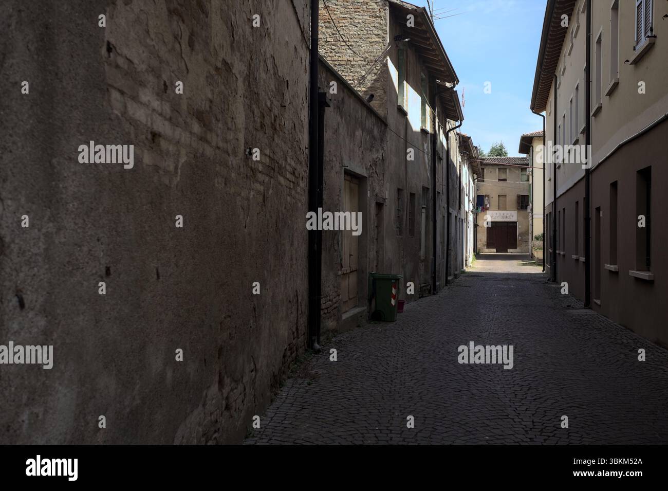 Vicolo all'ombra con un negozio abbandonato alla fine visto da un arco all'inizio della strada in una giornata di sole in una città italiana Foto Stock