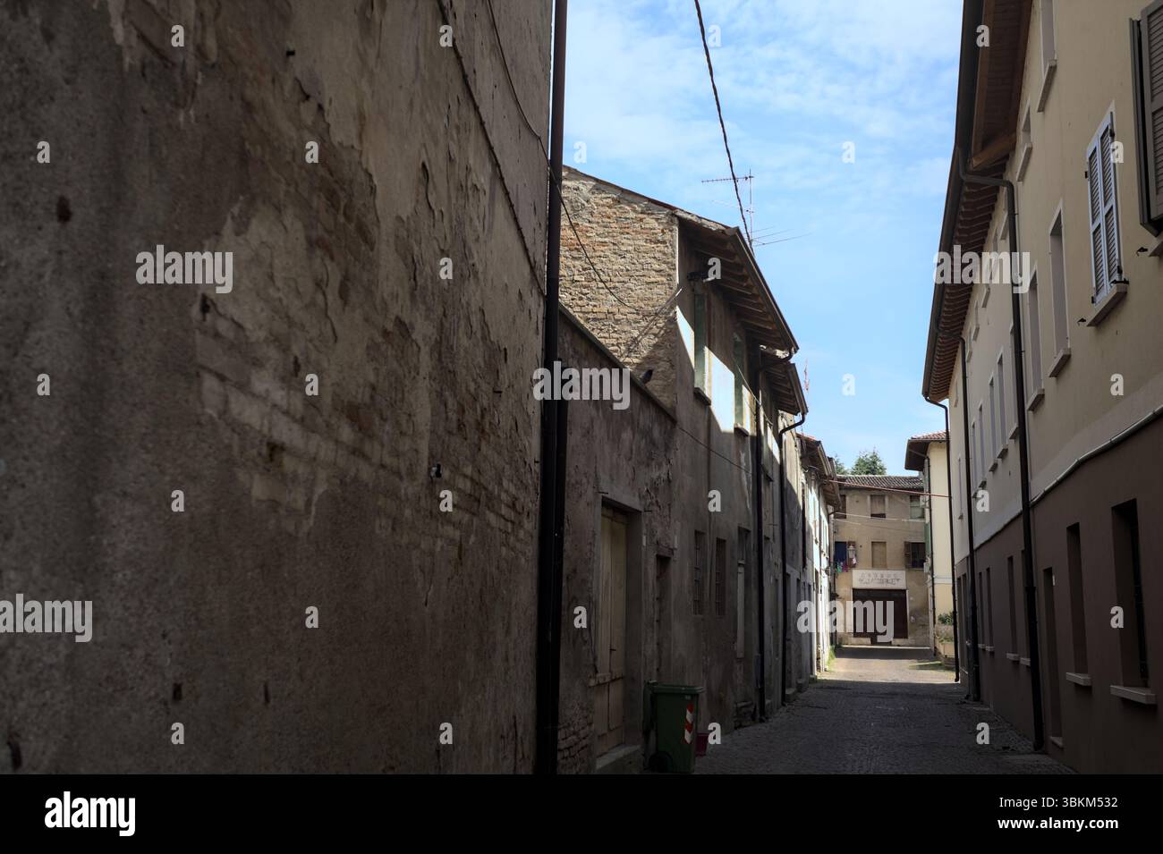 Vicolo all'ombra con un negozio abbandonato alla fine visto da un arco all'inizio della strada in una giornata di sole in una città italiana Foto Stock