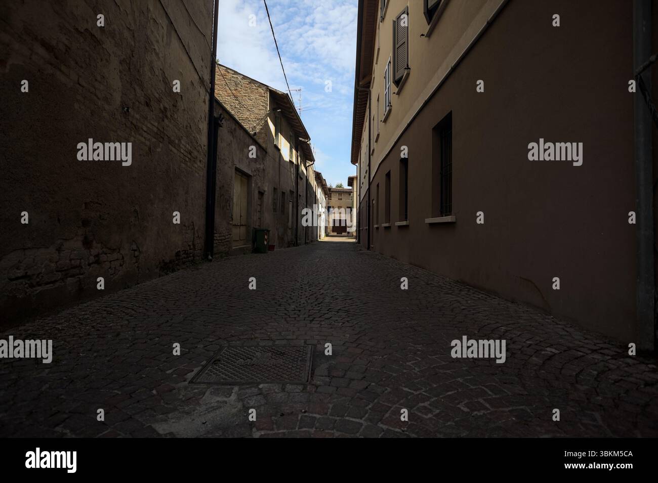 Vicolo all'ombra con un negozio abbandonato alla fine visto da un arco all'inizio della strada in una giornata di sole in una città italiana Foto Stock