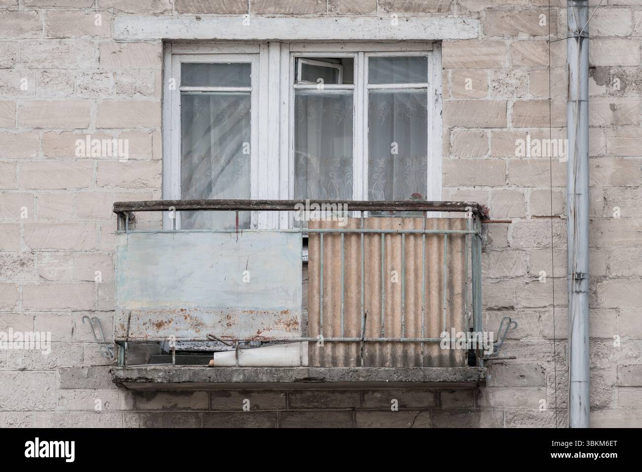 La facciata di un edificio intempestivo presenta un balcone fatiscente con ringhiera in metallo arrugginito. i toni tenui trasmettono il decadimento urbano, evocando sensazioni di solitudine Foto Stock