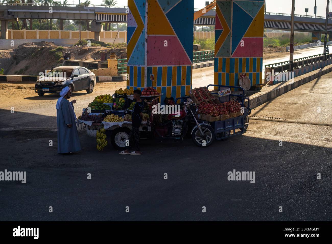 Cairo, Egitto - 11 settembre 2023: Un venditore ambulante che vende frutta fresca sotto pilastri dai colori vivaci, con uno sfondo egiziano urbano, raffigurante tra Foto Stock