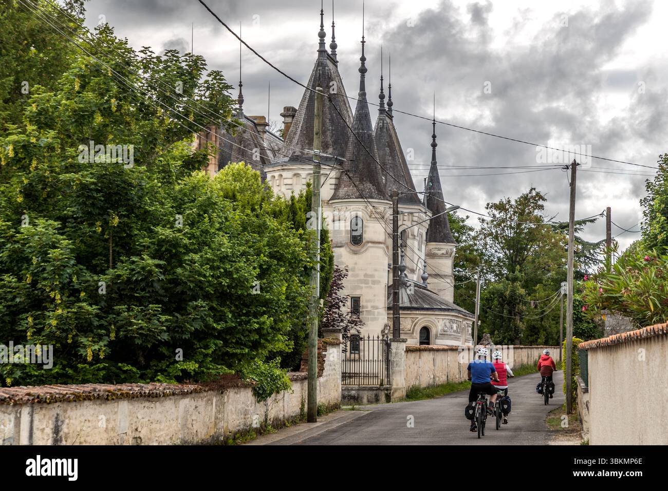 Un gruppo di ciclisti passa davanti all'Château Les Chabannes Chambres, un imponente edificio con torri. Pedalando attraverso il dipartimento della Charente sulla pista ciclabile Flow velo, passando per eleganti tenute di campagna e attraverso villaggi romantici. Rue des Chabannes, Jarnac, Nouvelle-Aquitaine, Francia Foto Stock