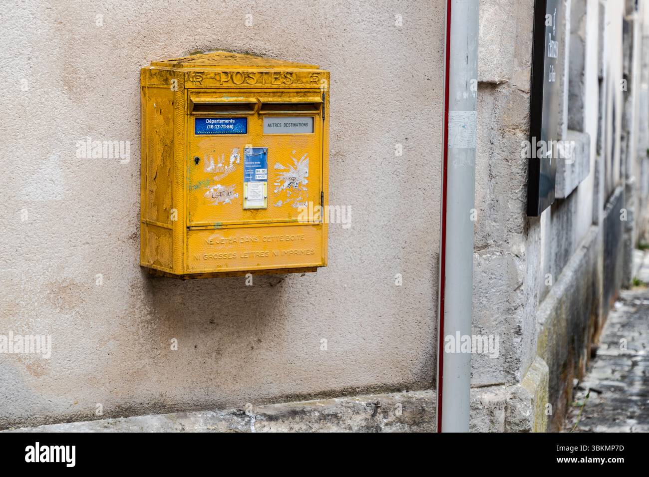 Una vecchia cassetta postale gialla è appesa a un muro in Rue Saulnier, Cognac, Nouvelle-Aquitaine, Francia, Europa. Riceve lettere e spedizioni postali, che l'ufficio postale poi raccoglie e consegna. La parola "POSTES" è incisa nel metallo in alto. Due fessure portano le diciture "Départements (16-17-79-86)" e "Autres destinations". In inglese: 'Départements 16, 17, 79, 86' e 'Other destinations'. I numeri indicano la Charente, la Charente-Maritime, i Deux-Sèvres e la Vienne, i quattro dipartimenti dell'ex regione Poitou-Charentes. Le lettere in rilievo in fondo leggono "Ne jeter dans cette boîte ni gro Foto Stock