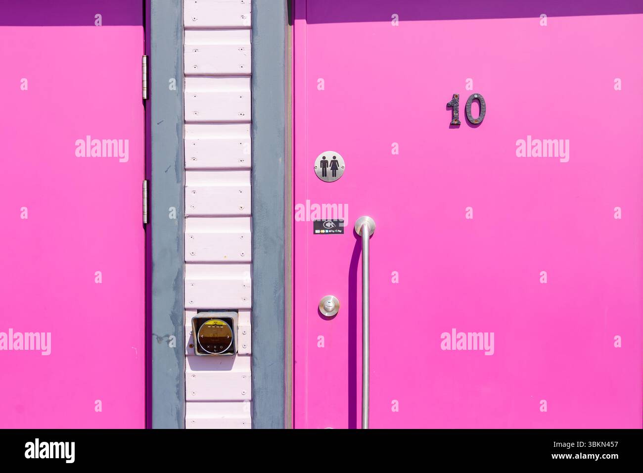 Porta del bagno pubblico rosa brillante con il numero 10 con maniglia argentata e simbolo del bagno con contactless senza contanti, rubinetto a pagamento, struttura seaton carew Foto Stock