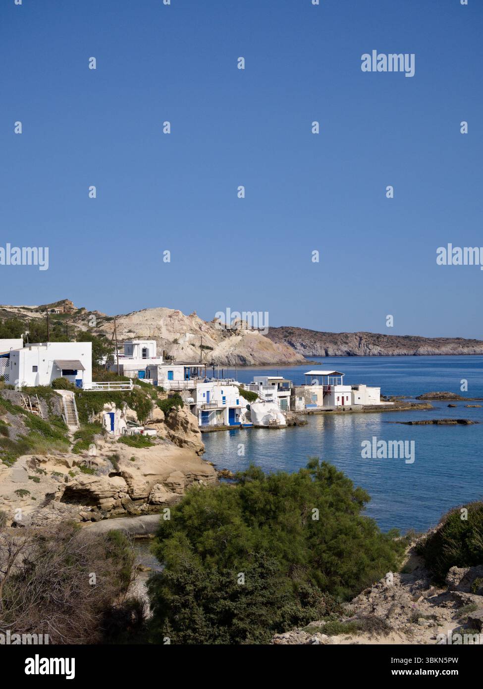 Vista distante di un tradizionale villaggio costiero greco sull'isola di Milos, caratterizzato da case bianche delle Cicladi lungo una costa rocciosa. Foto Stock