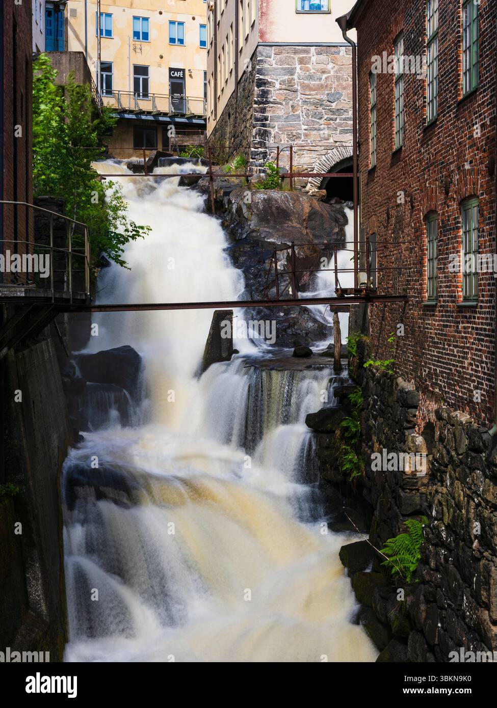 Una potente cascata scorre vigorosamente lungo le rocce accanto a uno storico edificio industriale a Mölndal, Svezia. Il contrasto tra natura e arcaite Foto Stock