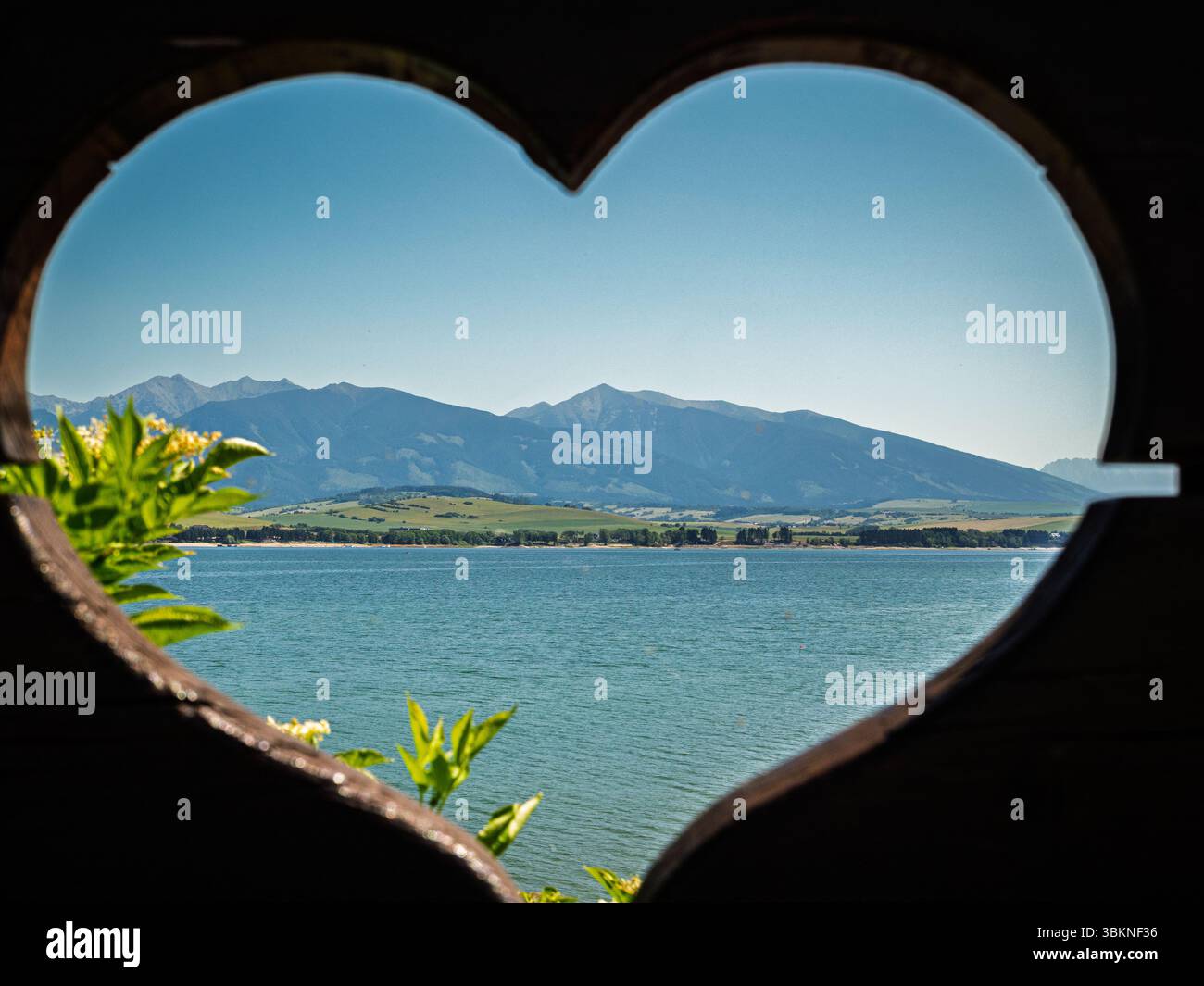 Vista di Kriváň e dei Tatra occidentali attraverso il cuore in legno intagliato a Dechtáre vicino a Liptovská Mara, vivace scena estiva Foto Stock