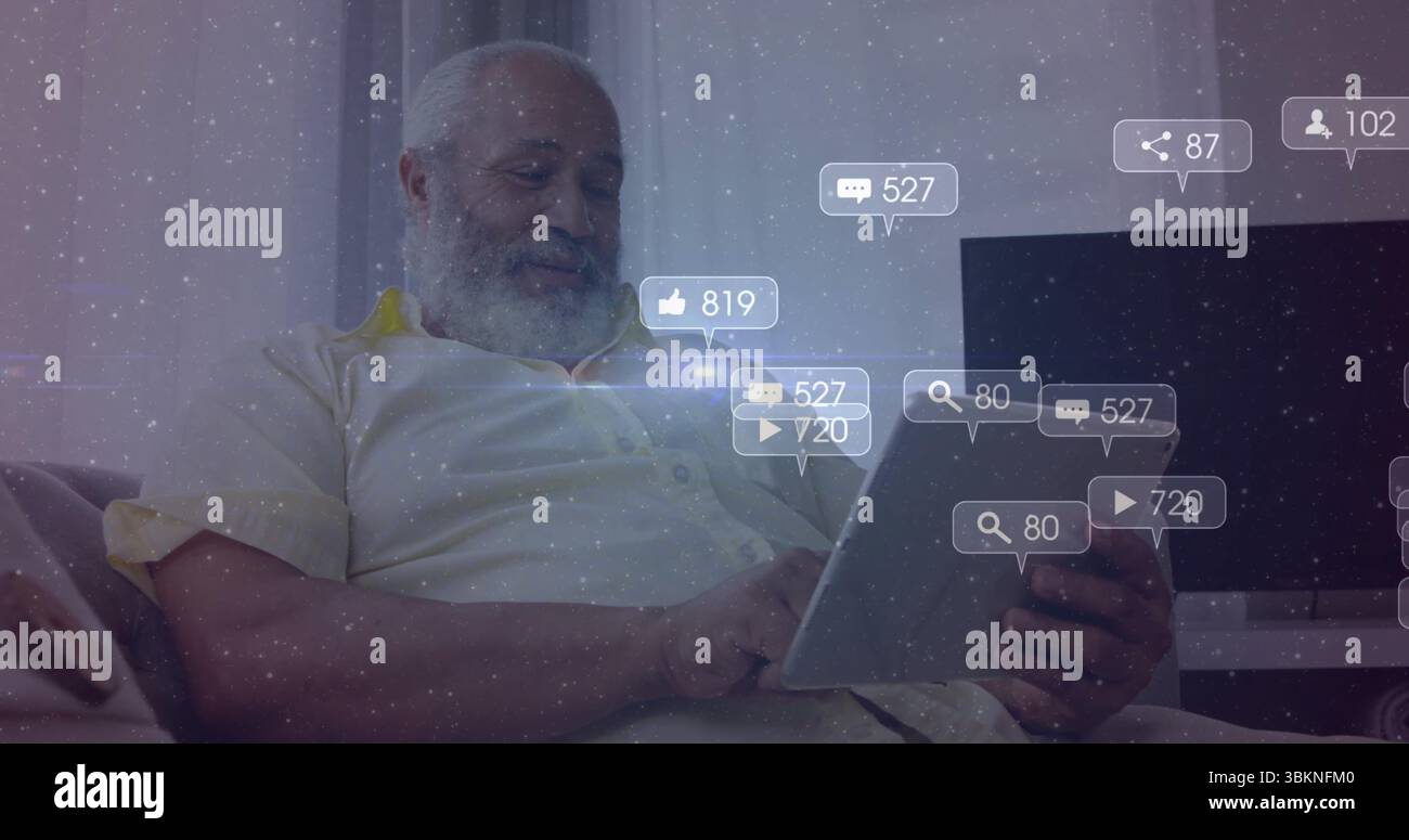 Uomo anziano del Medio Oriente che indossa una camicia pallida che tiene un tablet e guarda le icone fluttuanti nel soggiorno Foto Stock