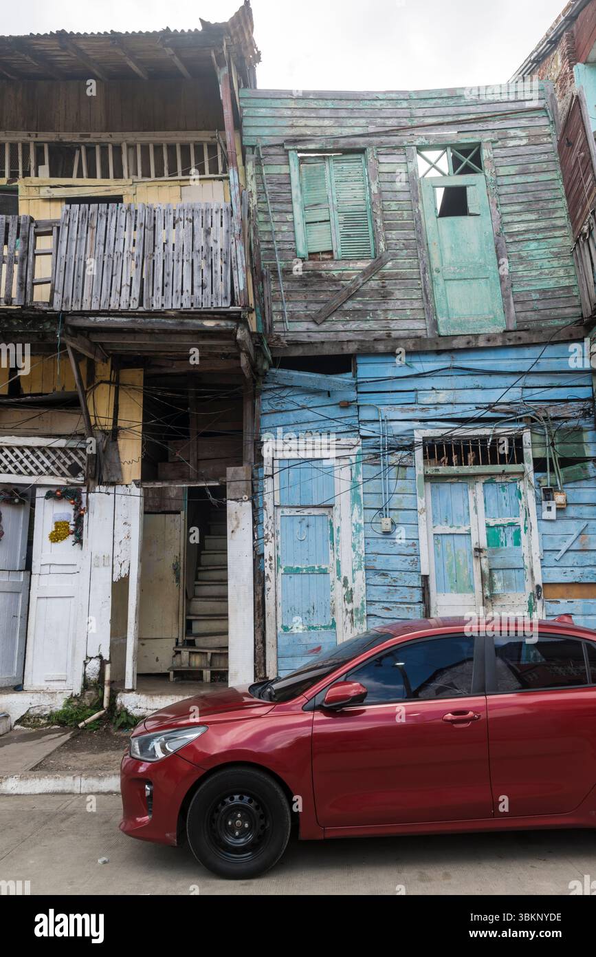 Auto rossa di fronte ad una casa completamente fatiscente dipinta in diversi colori pastello. Casco Viejo, Panama City, Panama Foto Stock