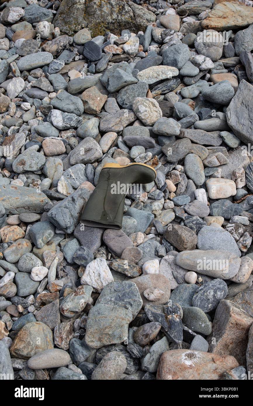 Un unico stivale verde abbandonato Wellington sulle rocce di una spiaggia in Cornovaglia, Inghilterra Foto Stock