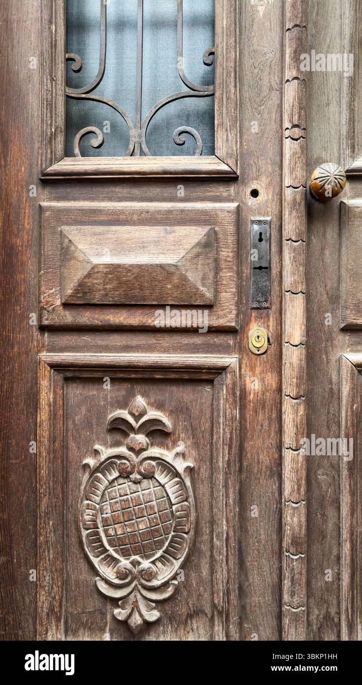 Dettaglio della porta in legno vintage con intagli ornamentali, griglia in ferro e struttura rustica. Ideale per sfondi o grafica architettonica. Foto Stock