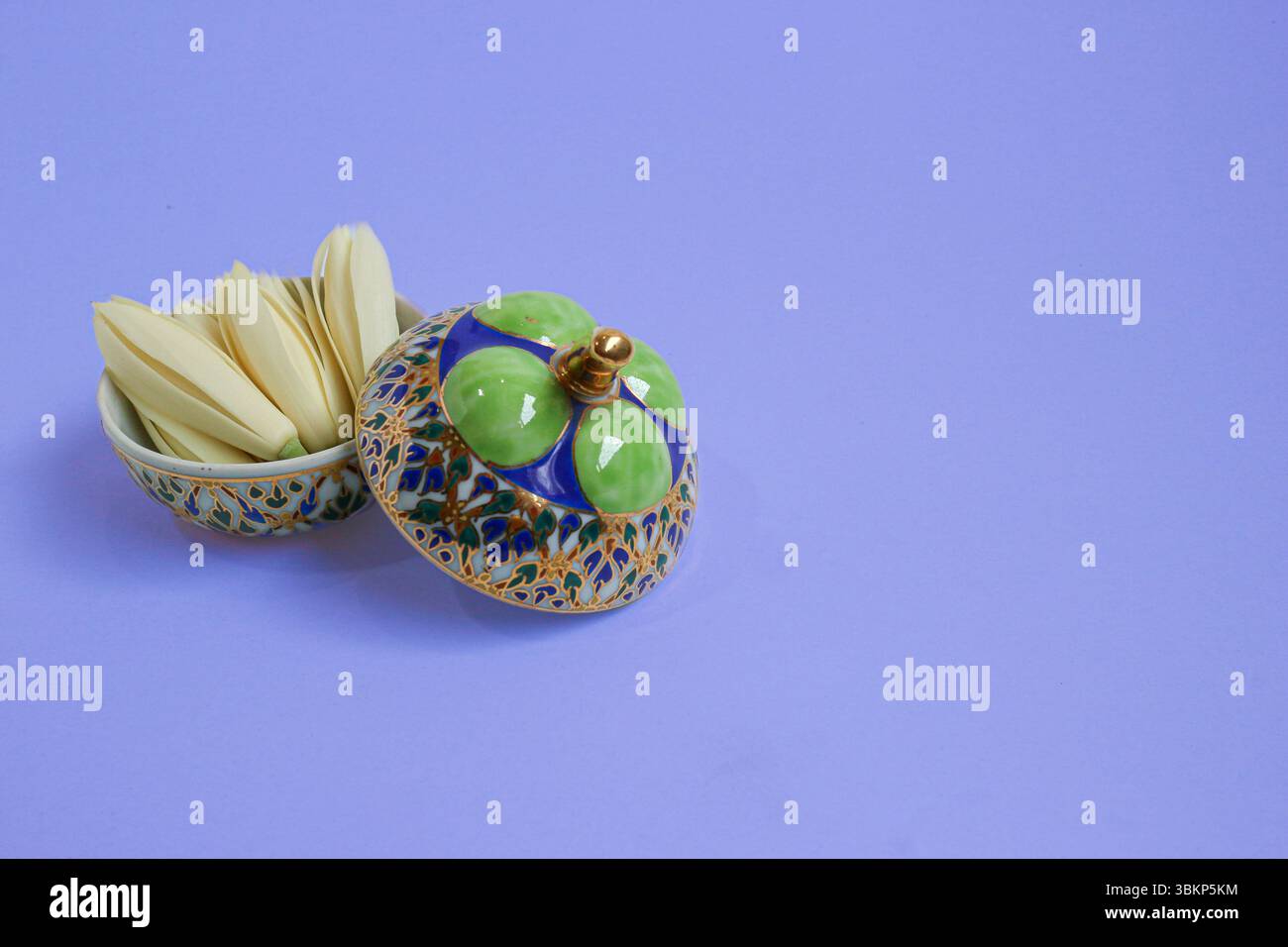 Elegante mangostano in ceramica lavorato a mano con finiture dorate, aperto per rivelare un fiore profumato all'interno. Posizionato a sinistra con spazio per testo creativo. Foto Stock