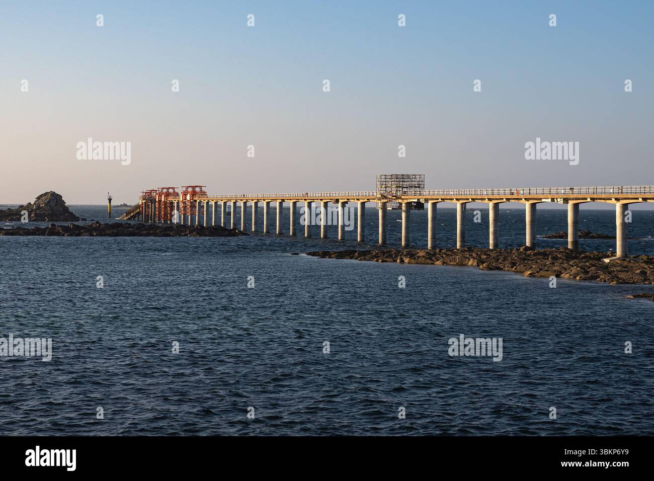La luce dorata della sera illumina il pontile dell'estacade di Roscoff, Bretagna, utilizzato per le navette per Île de Batz, con un mare calmo e un cielo limpido. Foto Stock