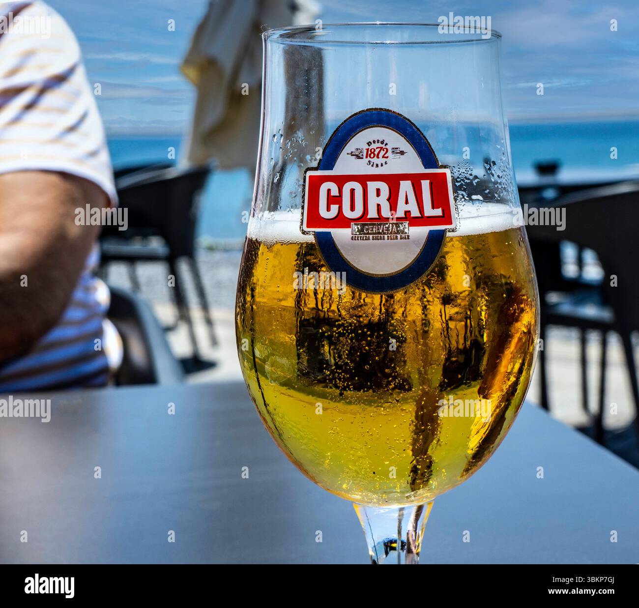 Un bicchiere di birra di corallo ghiacciata, una lager locale di Madeira, su una terrazza sul mare con vista sull'oceano e rilassata atmosfera estiva, perfetta per rinfrescarsi le vacanze Foto Stock